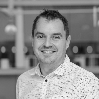 Black and white image of a man standing side profile wearing a patterned white collared shirt called Chris Garratty
