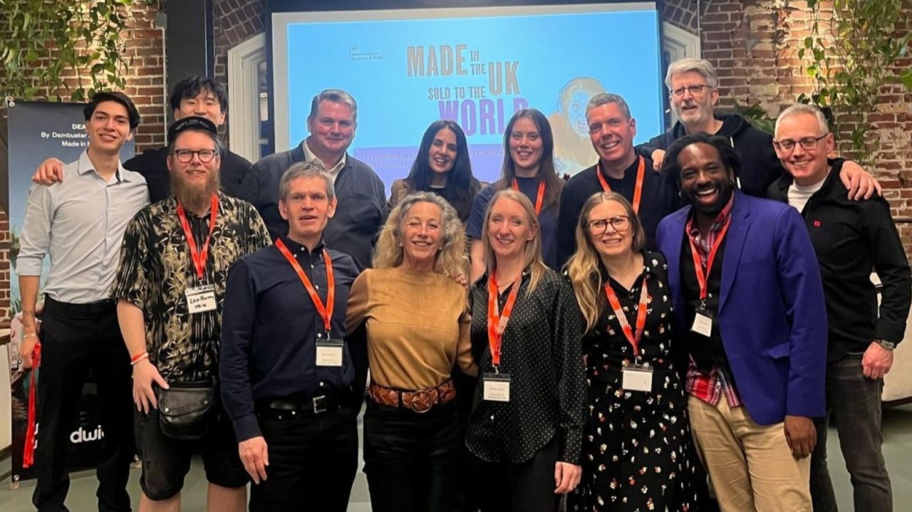 Group of people standing in front of a display with the text 'Made in the UK Sold to the World' all smiling at the camera