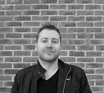 Black and white headshot of a man standing against a brick wall called Mark Slaughter