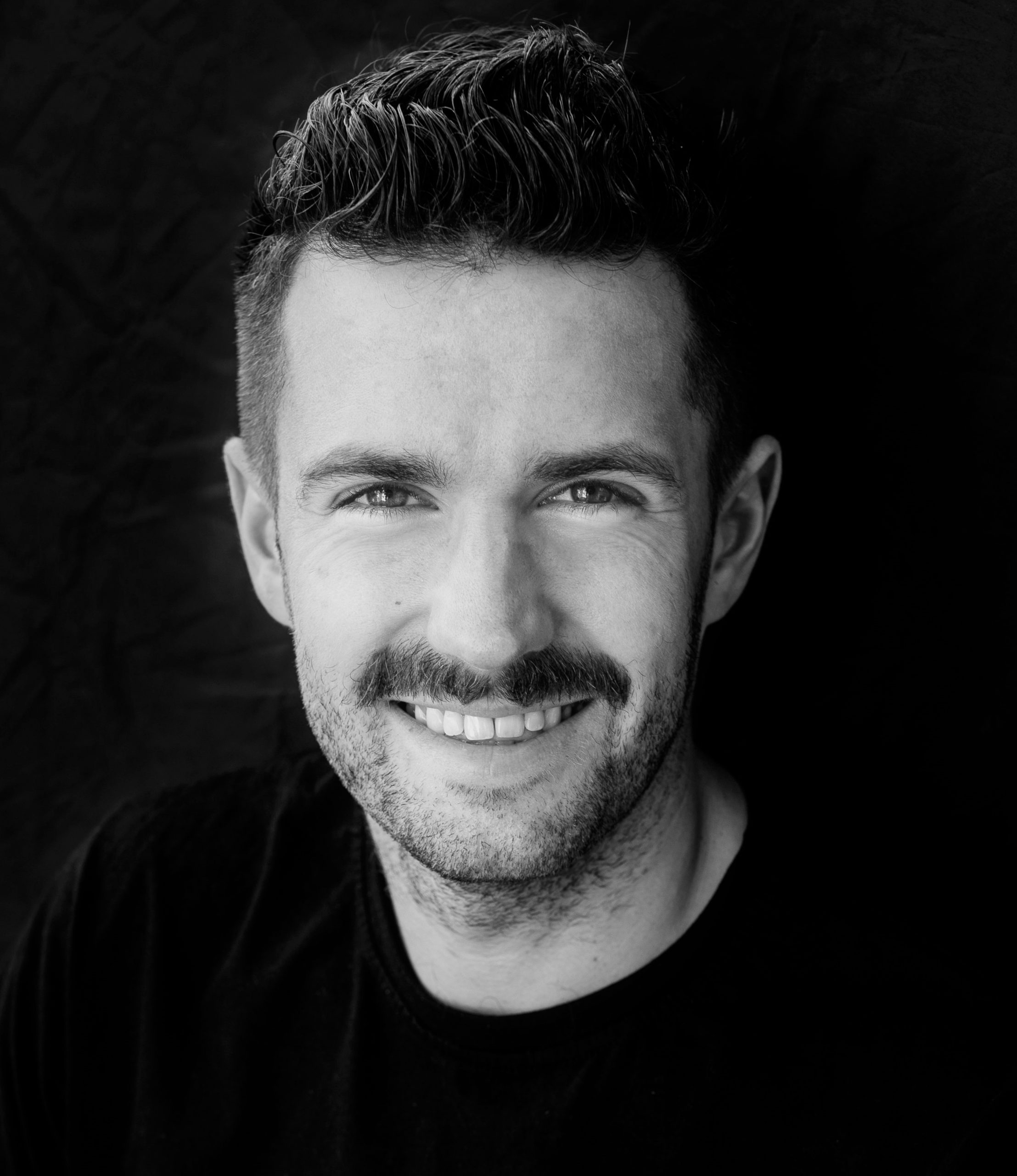 Black and white image of a bearded man smiling at the camera. His name is Rafal Kloczko