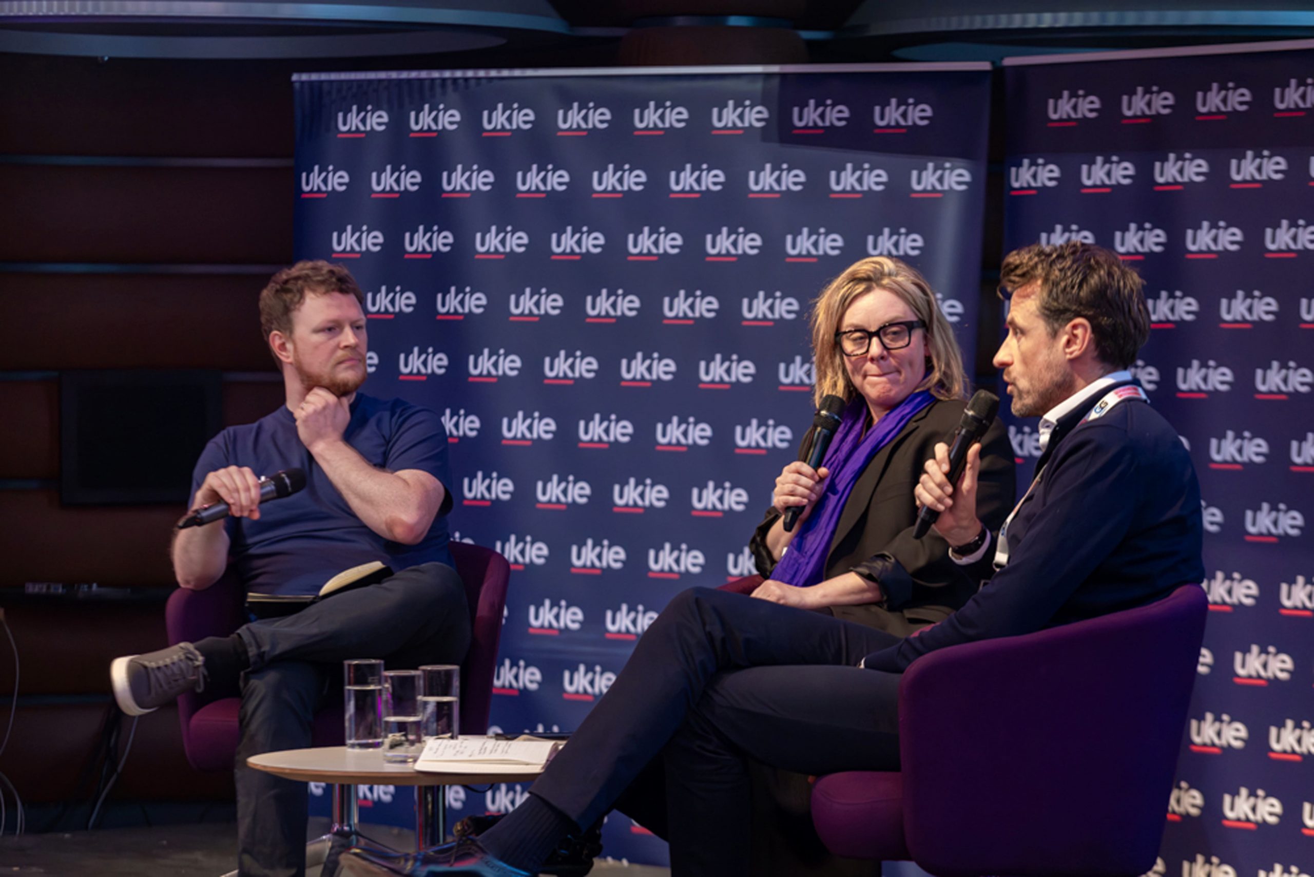 Two male and one female professionals sitting on a seats doing interviews at Ukie members day 2025