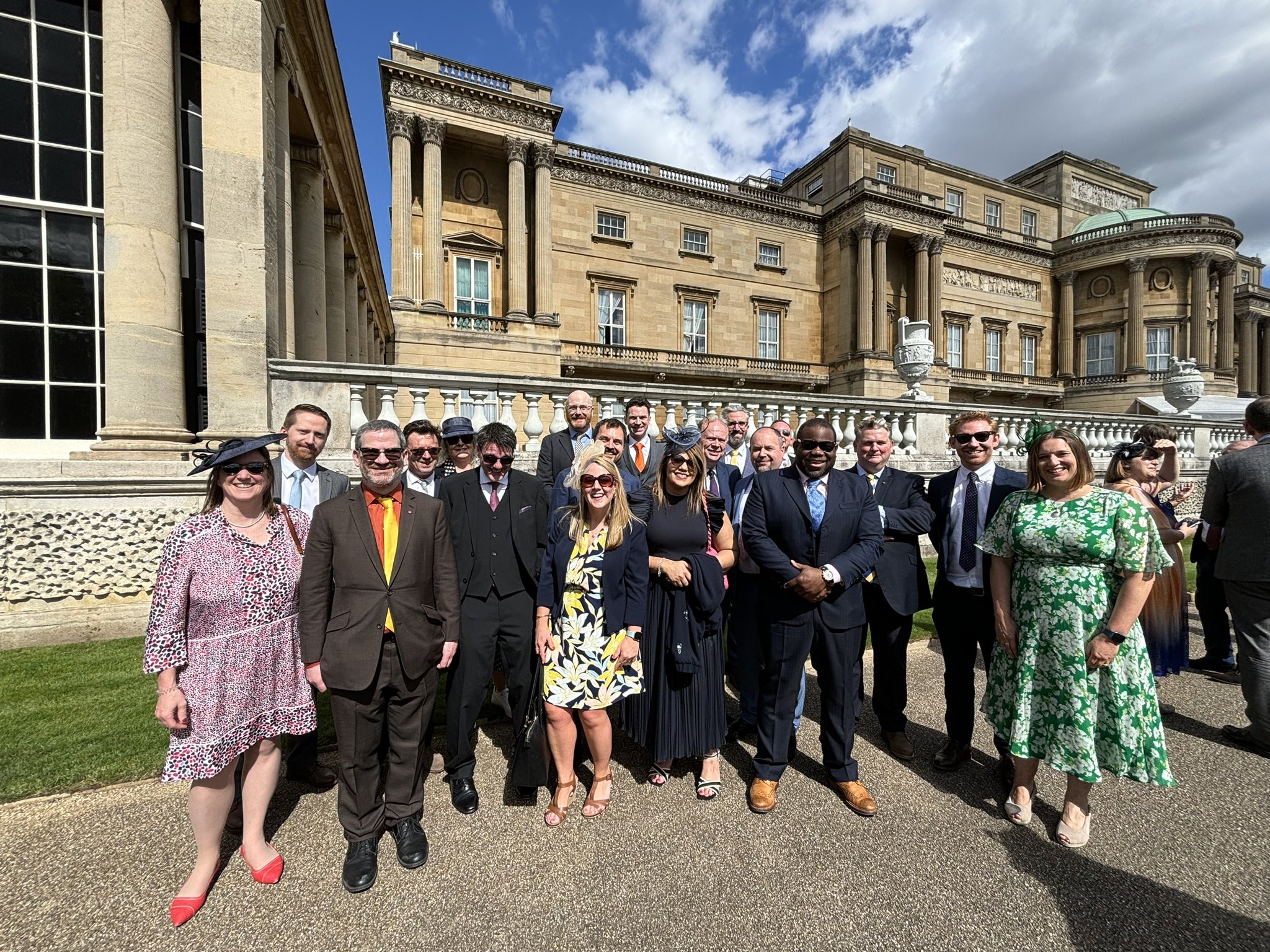A group of professionals standing in the sunshine outside a building having a garden party